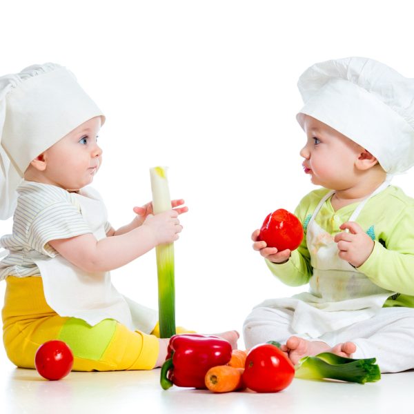 dve deti s kuchárskymi čiapkami na hlave jedia zdravú zeleninu