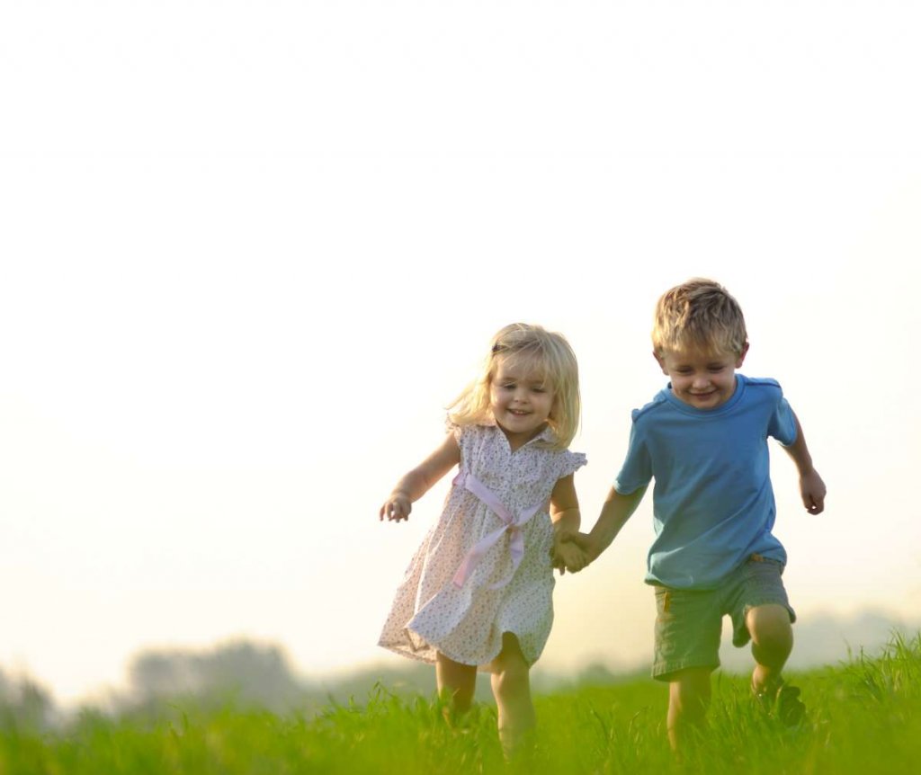 chlapček a dievčatko bežia po zelenej lúke držiac sa za ruky